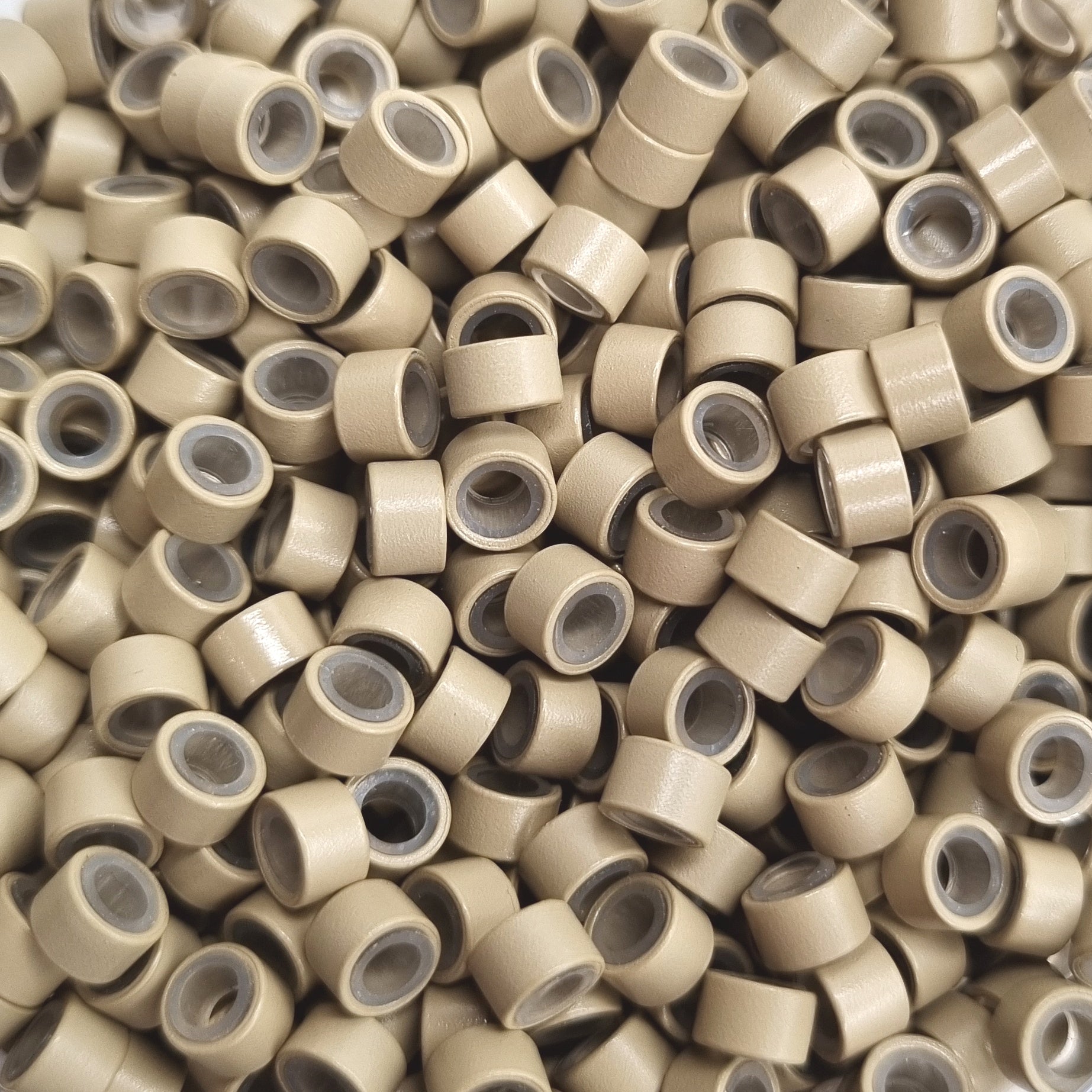 Close up of salon professional silicon lined aluminium Blonde micro beads used as an anchor for weave hair extensions. The silicone lining provides extra grip and acts as a soft, protective layer between the bead and natural hair.