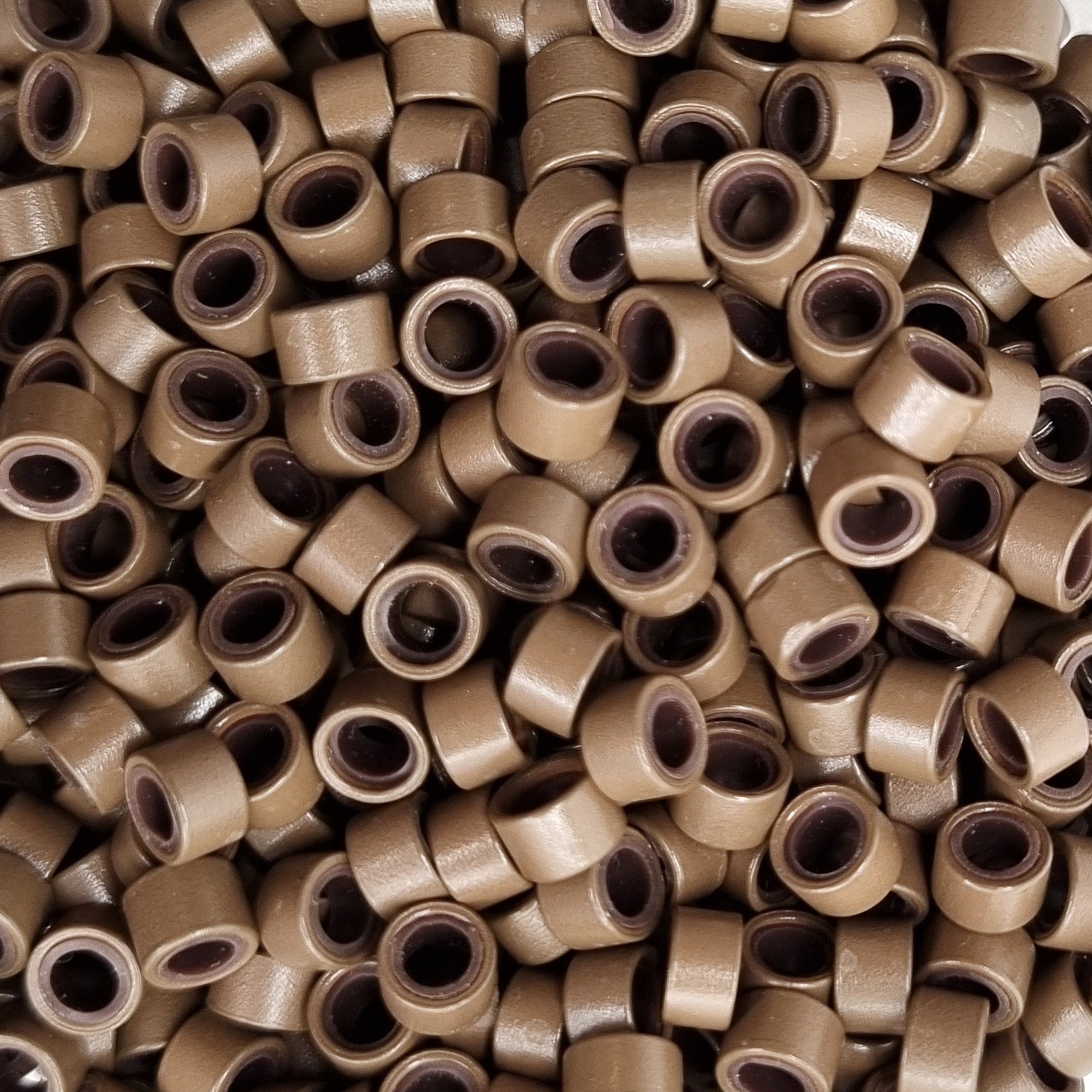 Close up of salon professional silicon lined aluminium Light Brown micro beads used as an anchor for weave hair extensions. The silicone lining provides extra grip and acts as a soft, protective layer between the bead and natural hair.