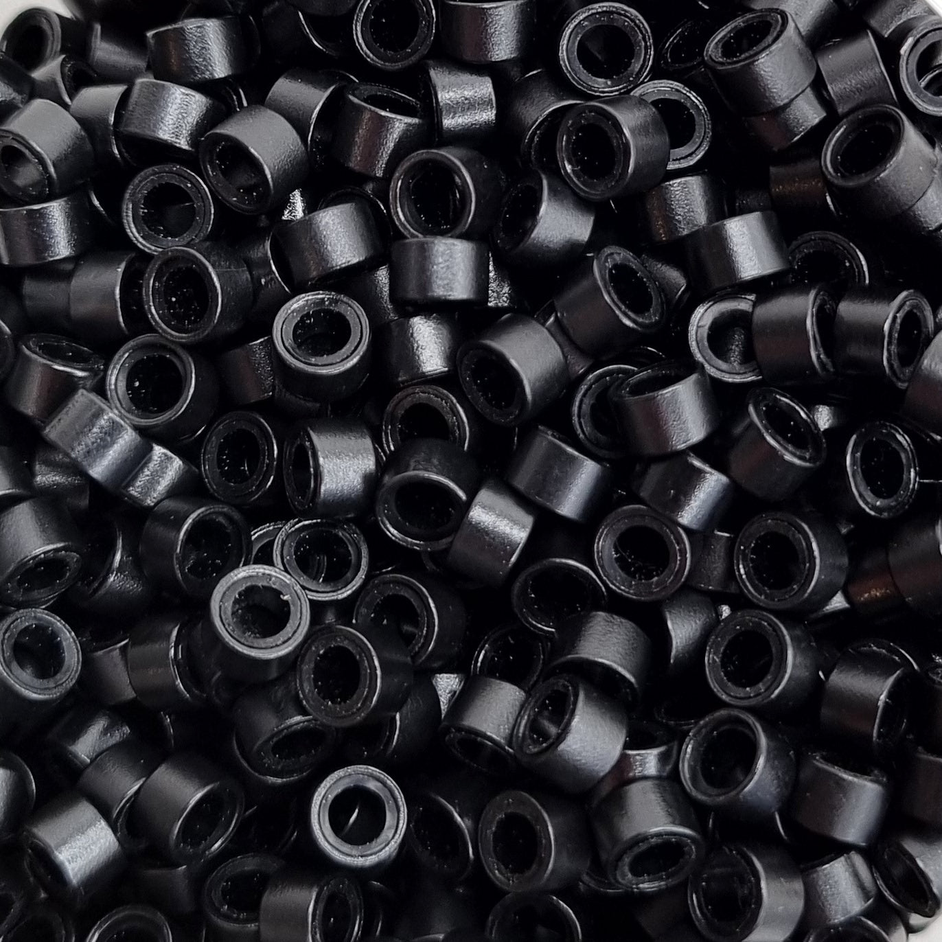 Close up of salon professional silicon lined aluminium Black micro beads used as an anchor for weave hair extensions. The silicone lining provides extra grip and acts as a soft, protective layer between the bead and natural hair.
