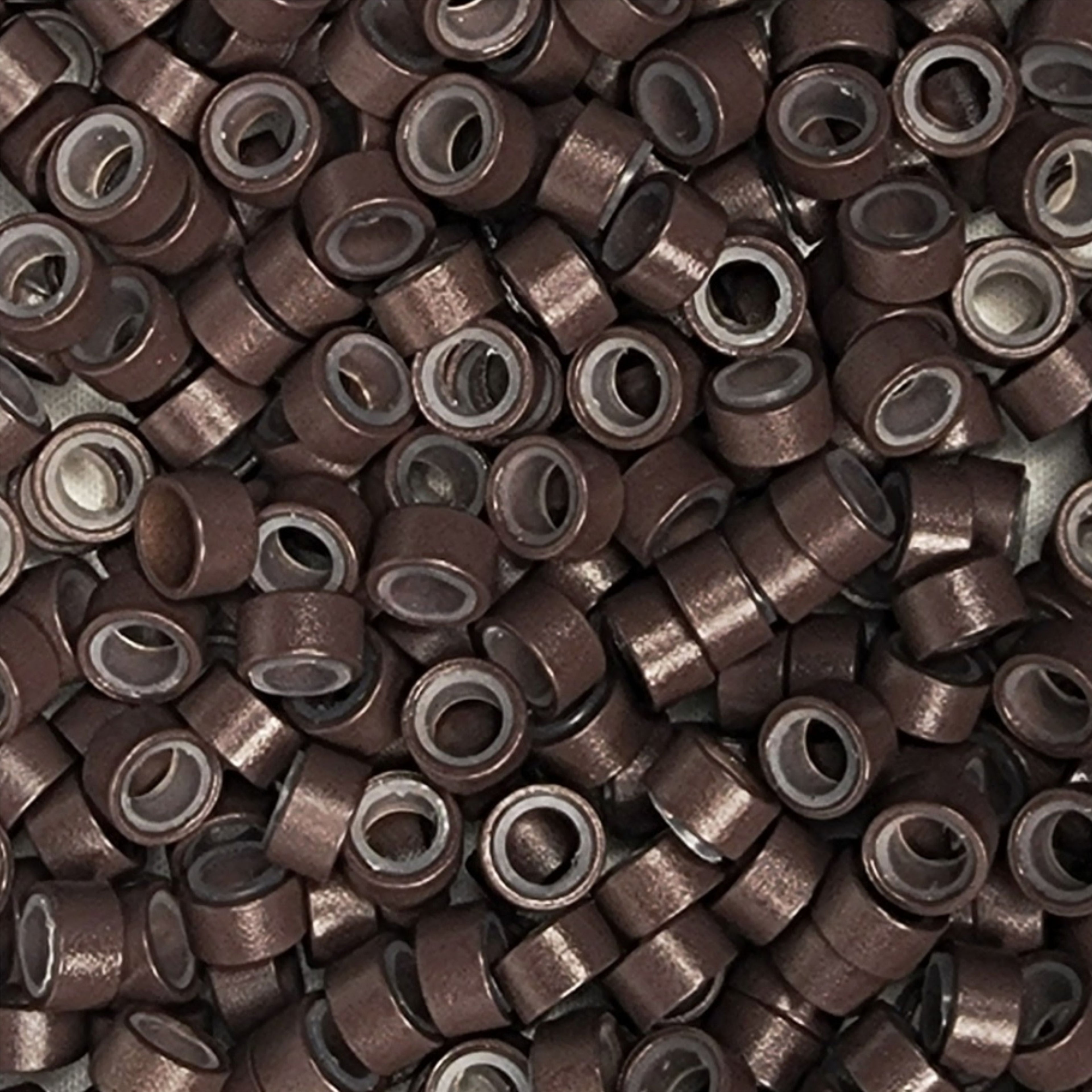 Close up of salon professional silicon lined aluminium Dark Brown micro beads used as an anchor for weave hair extensions. The silicone lining provides extra grip and acts as a soft, protective layer between the bead and natural hair.